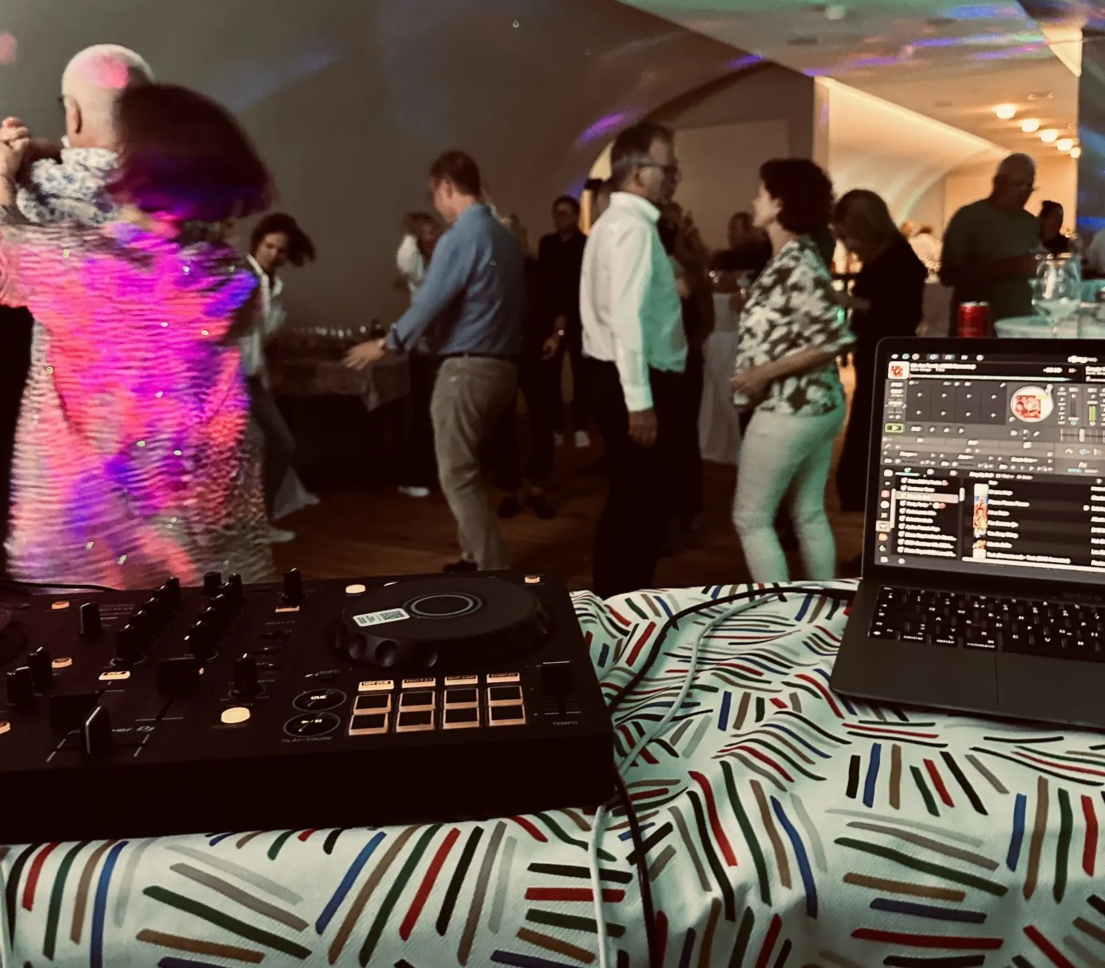 DJ-Controller, dahinter tanzende Paare im Saal