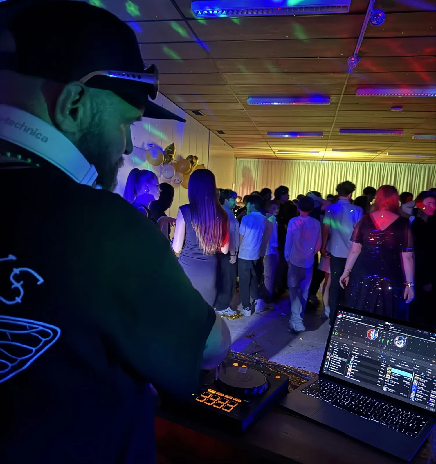 Blick über das DJ-Pult in einen Saal mit Tanzenden